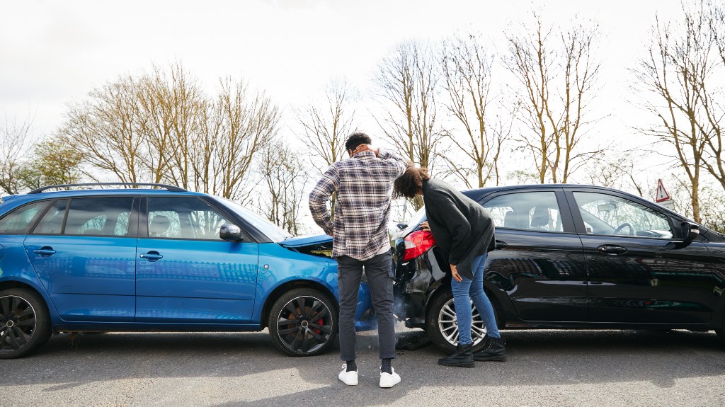 Young male and female drivers looking at damaged car