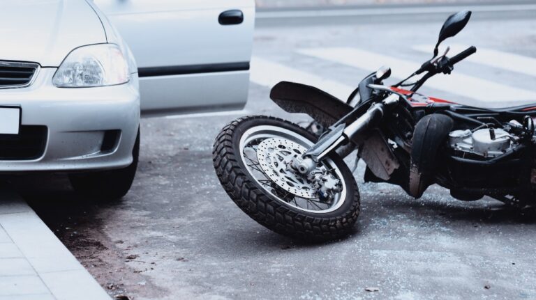 A motorcycle lying on the road and a car standing with the door open