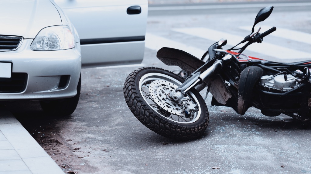 A motorcycle lying on the road and a car standing with the door open