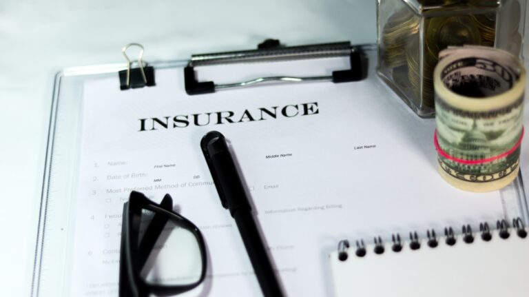 Insurance form with can of coins and dollar bundle with a pen and eyeglass
