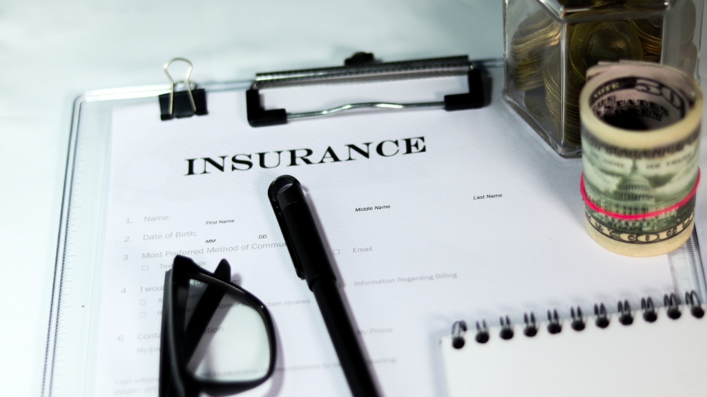 Insurance form with can of coins and dollar bundle with a pen and eyeglass