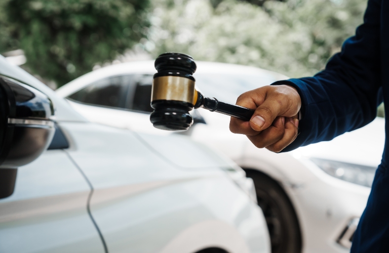 lawyer holding a wooden gavel and standing in front of a car